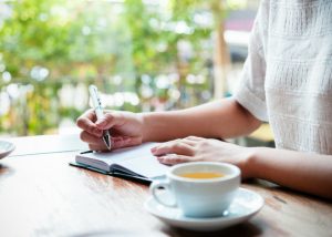 a woman writing in her diary with a cup of tea at the side