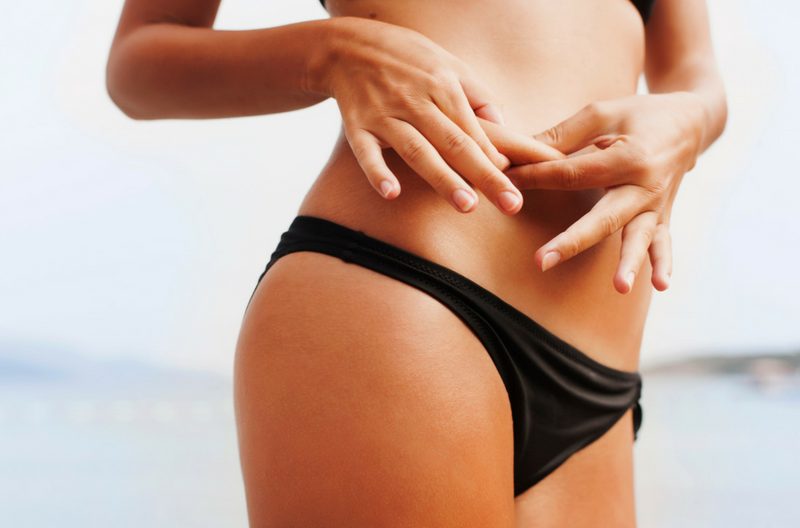 A toned woman in a bikini pinching flab on her tummy