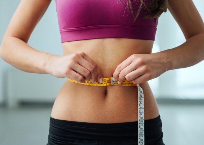 a woman in workout clothes measuring her waist with a tape measure