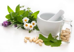 ginkgo biloba leaves, herbs, flowers, pestle and mortar as well as supplement capsules on a table