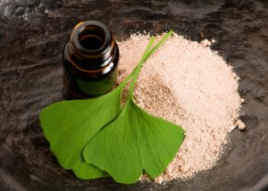 ginkgo biloba leaves, ginkgo biloba powder and a brown bottle on a wooden table