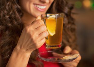 woman smiling and holding a glass of lemon and ginger tea