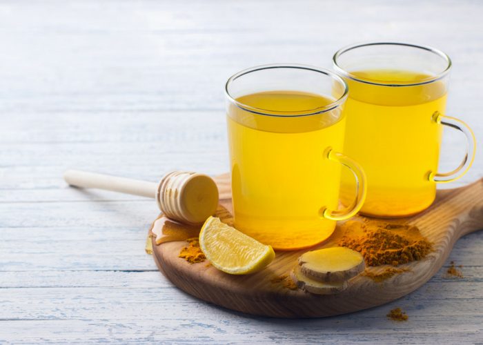two glasses of turmeric ginger honey tea on a wooden board