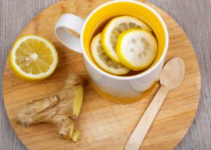 top down view of a mug of lemon and ginger tea on a wooden board with half a lemon and fresh ginger on the side