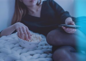 a woman watching tv and eating popcorn