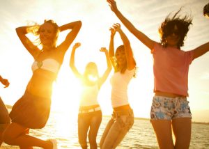 a group of girls dancing on the beach at sunset