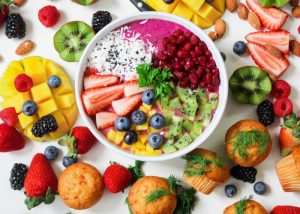 a healthy fruit bowl with strawberries, mangoes, kiwis, blueberries, pomegranate seeds, and lots of other fruits around it on a table