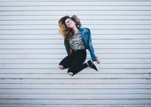 a woman in a denim jacket and sunglasses jumping for joy