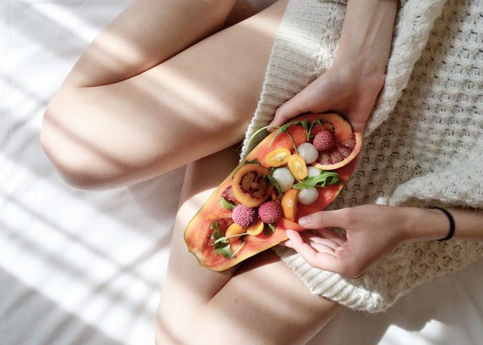 a woman holding half a papaya with small fruits on top of it