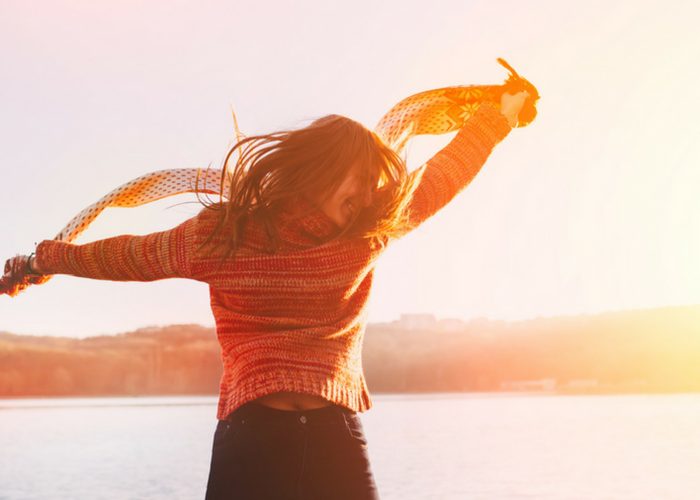 a happy woman dancing with a scarf at sunset