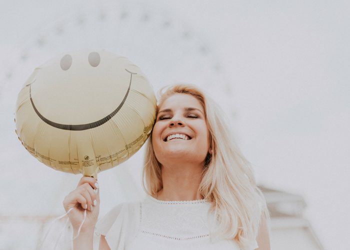 a woman at a carnival smiling and holding a smiley face balloon