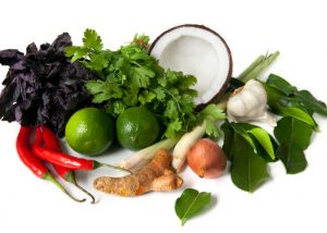 fresh ingredients for a curry such as chilis, cilantro, coconut, ginger, garlic, onions