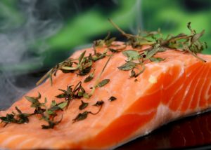 close up of a salmon fillet sprinkled with thyme leaves cooking on a pan