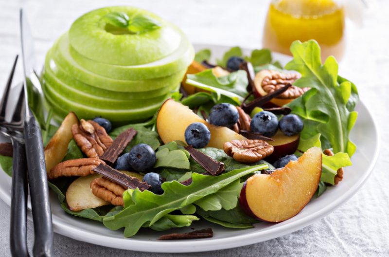 Plate of alkaline diet foods such as apple, blueberries, dark leafy greens, and nuts