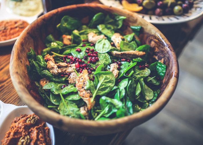 a wooden bowl with spinach salad, grilled chicken slices, and pomegranate seeds