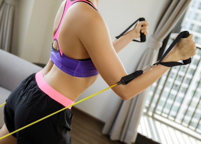 woman doing reverse pectoral fly chest exercises at home with a resistance band