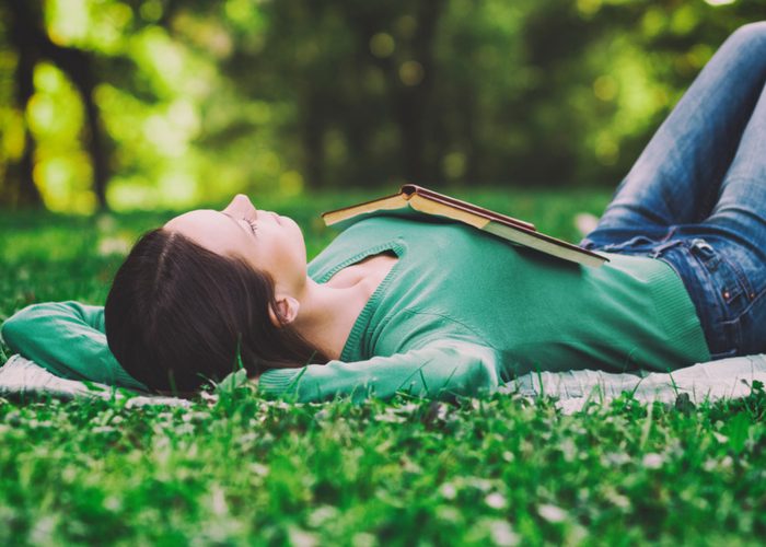 woman lying on the grass with her eyes closed and an open book on her chest