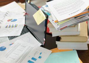 a messy pile of paper documents on a table covering a laptop