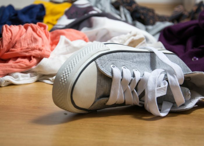 grey shoe on the floor with a messy clutter of clothes behind it