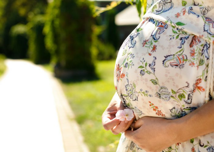 closeup of pregnant woman in floral dress holding a flower under her belly