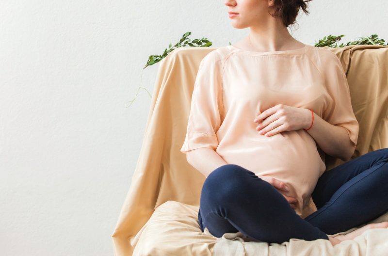 Woman in sweater and jeans holding her pregnant belly