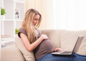 pregnant woman on a couch looking at her laptop and holding her belly
