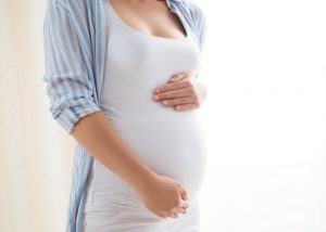 pregnant woman in white top and striped shirt holding her belly