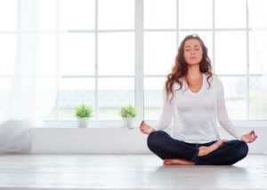 woman in a white shirt meditating in a light filled room