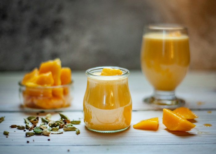 a dish with chopped mangos, a glass of mango smoothie, and a jar of mango smoothie