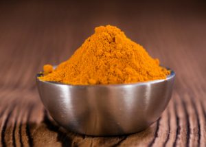 a bowl of heaped turmeric powder on a wooden table