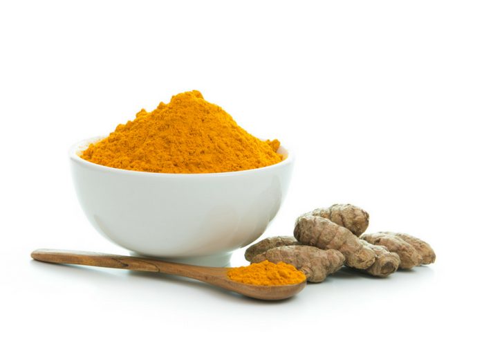 turmeric powder in a white bowl and wooden teaspoon and fresh turmeric on the side