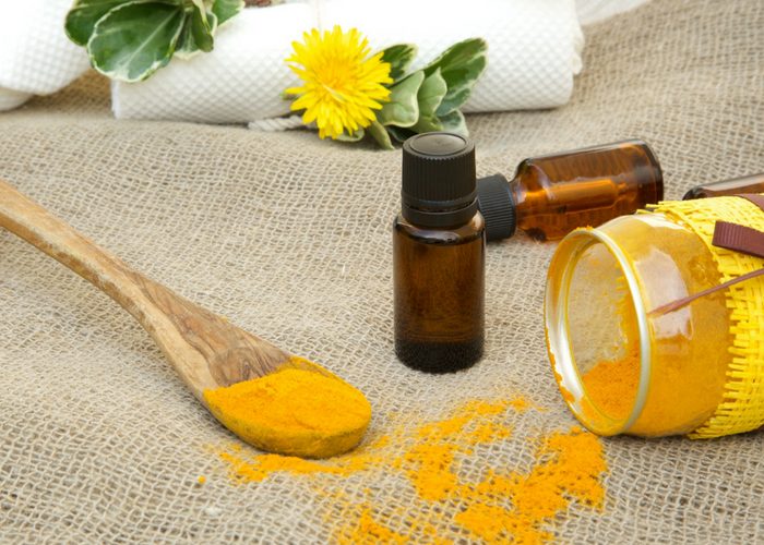 turmeric oil in brown vials, turmeric powder on a wooden spoon and turmeric powder in a jar