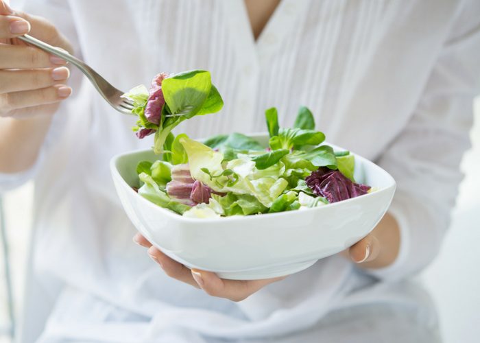 woman holding up a fork and a bowl of green salad