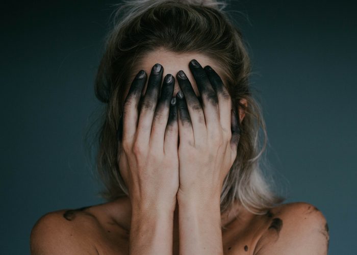 woman covering her face with with blackened fingers 