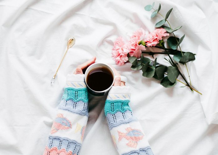 woman in knitted sweater holding a cup of tea with flowers next to her