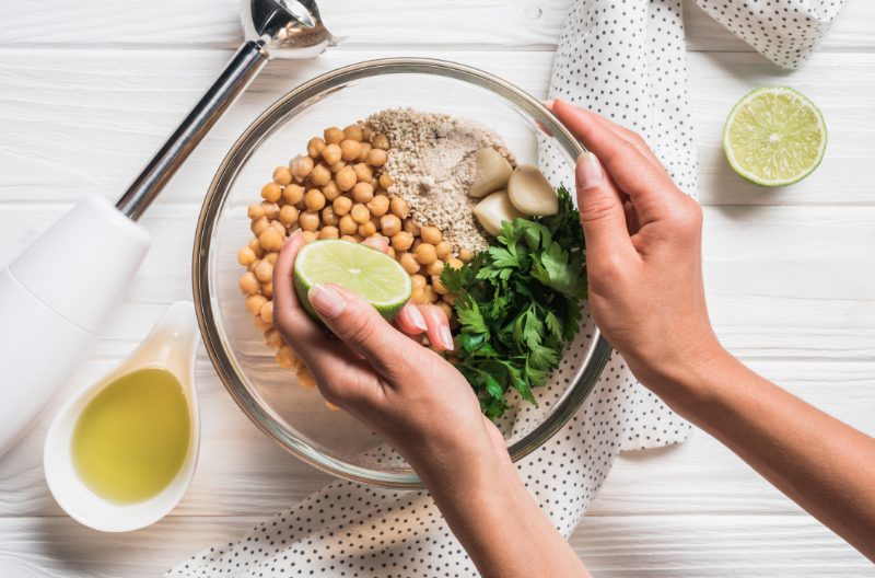 Woman squeezing lime into a bowl of vegan hummus ingredients with a blender by the side