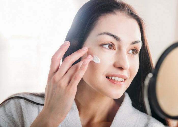 woman looking into a mirror applying barrier cream as part of her best skin care routine