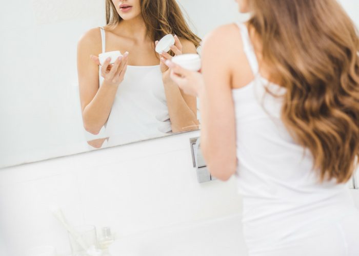 woman holding an open jar of skin care cream in her bathroom