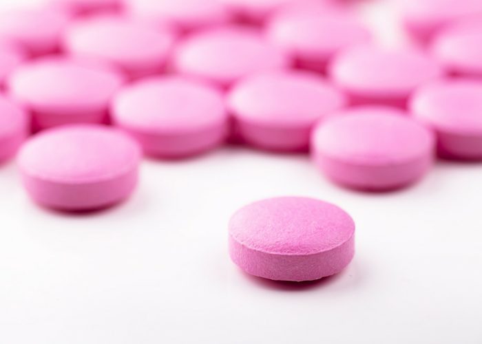 a bunch of pink pill supplements on a white table with a close-up on just one of them