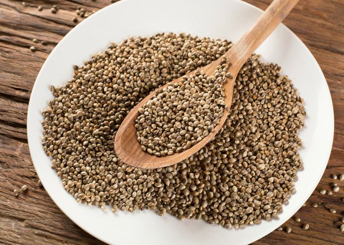 whole hemp seeds and wooden spoon on a white plate