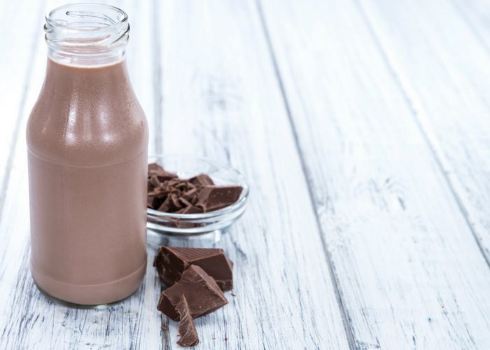 a bottle of cocoa hemp milk on a white table and a bowl of chocolate pieces next to it