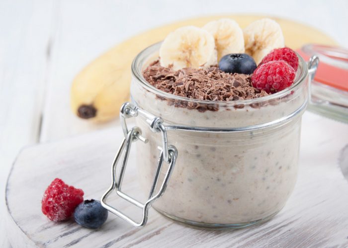 a jar of chia and hemp overnight oats topped with bananas, chocolate flakes, blueberries, and raspberries