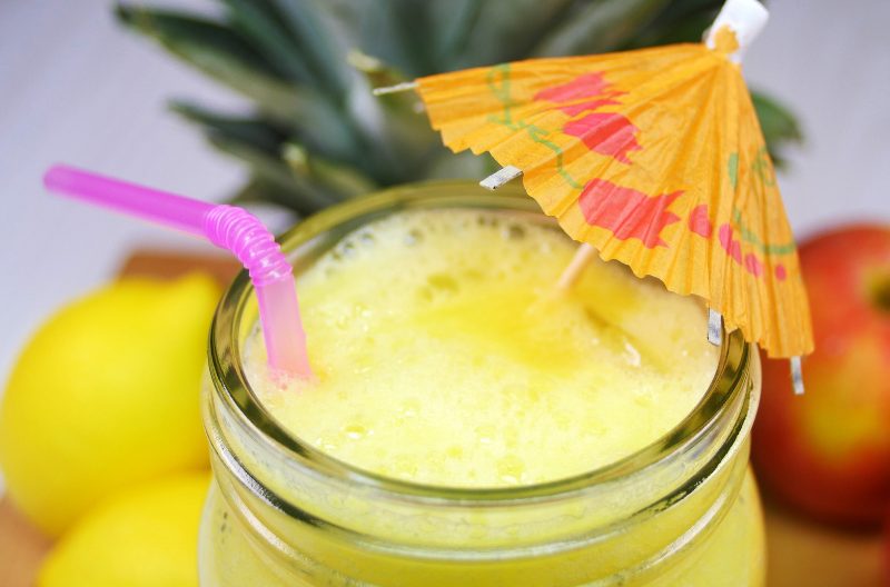 Bright yellow homemade energy drink in a mason jar with a tropical umbrella and pink straw