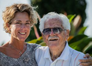 a centenarian in sunglasses with his daughter standing beside him