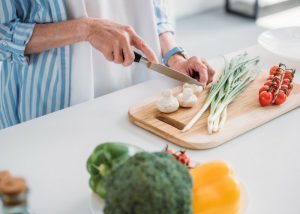 elderly woman cooking chopping fresh vegetables on a wooden chopping board