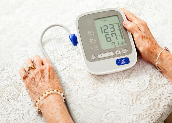 an old woman using a blood pressure machine at home