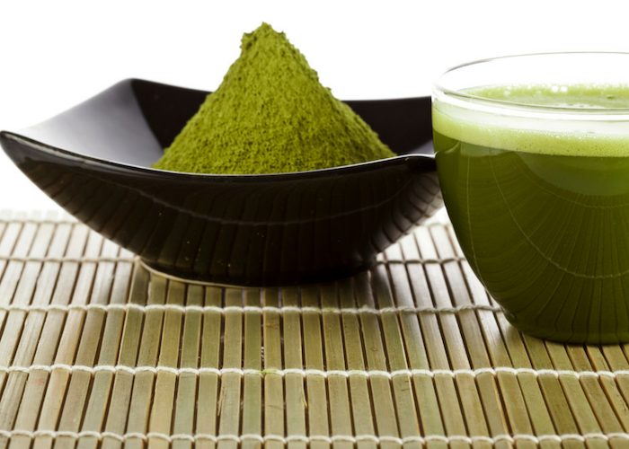 matcha green tea powder heaped in a black dish, with a clear glass of matcha green tea beside it