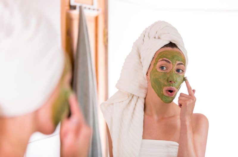 Woman applying a matcha green tea face mask in the bathroom mirror