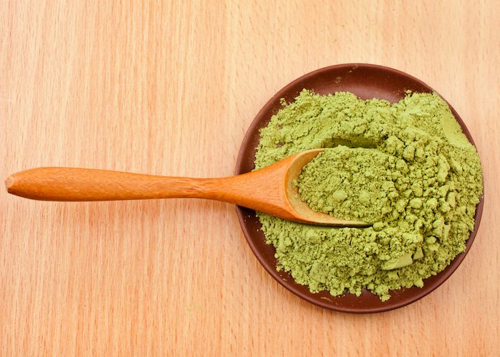 matcha green tea powder on a wooden spoon, in a lacquer dish on a wooden table