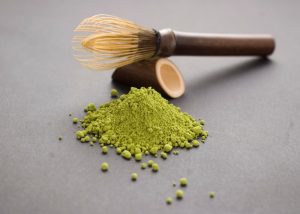 matcha green tea powder on a grey tabletop with a bamboo whisk